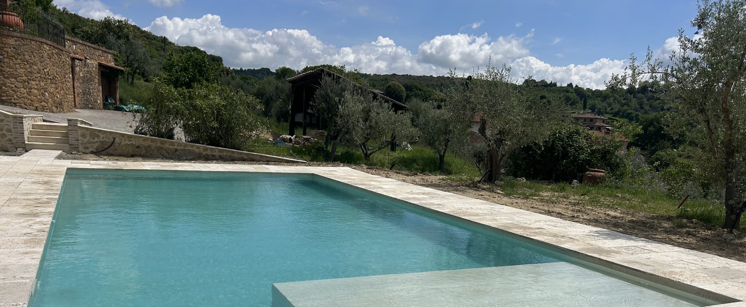 Piscina con bordo in travertino tra gli ulivi