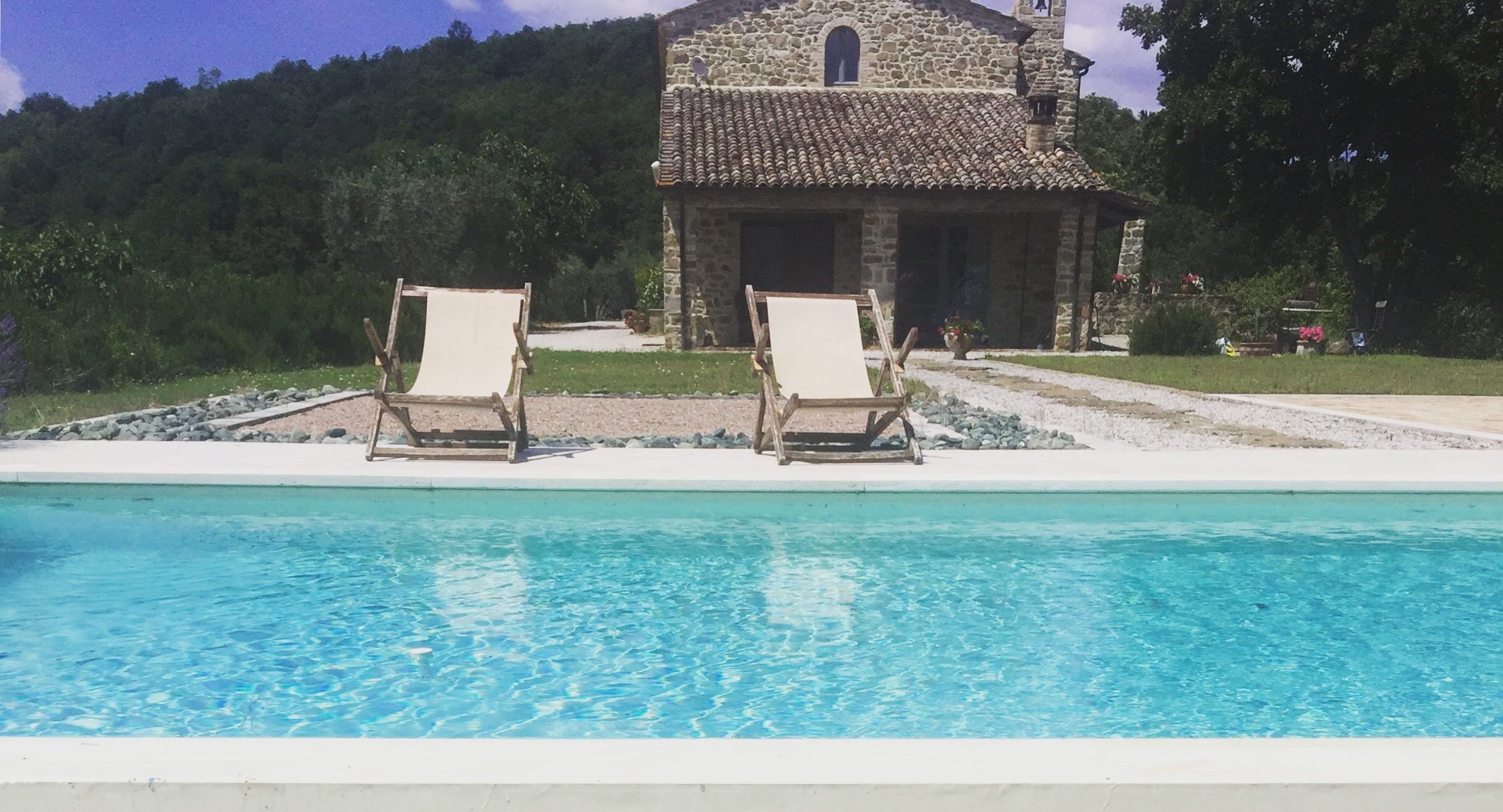 Piscina con due sdraio e un casale in pietra