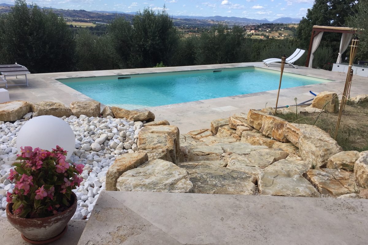 Piscina interrata tra rocce e ulivi con vista sulle colline umbre