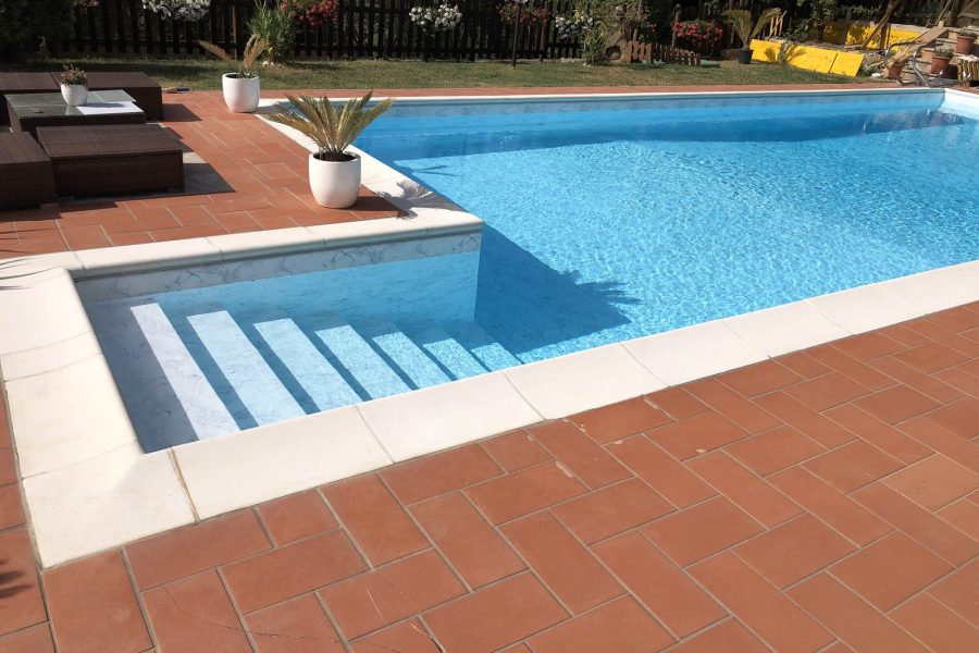 Piscina in mosaico azzurro con bordo bianco e pavimentazione in cotto