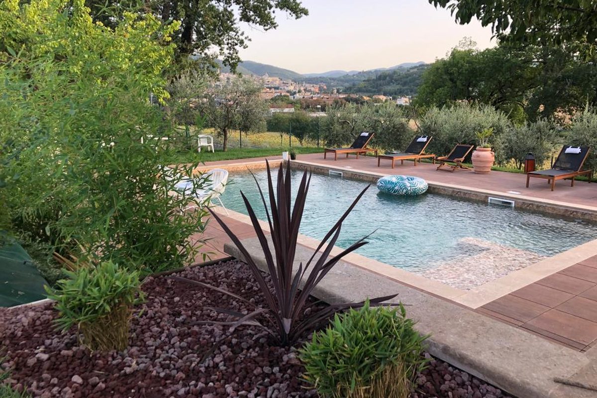 Piscina con vista su Spoleto tra piante e prato, al tramonto