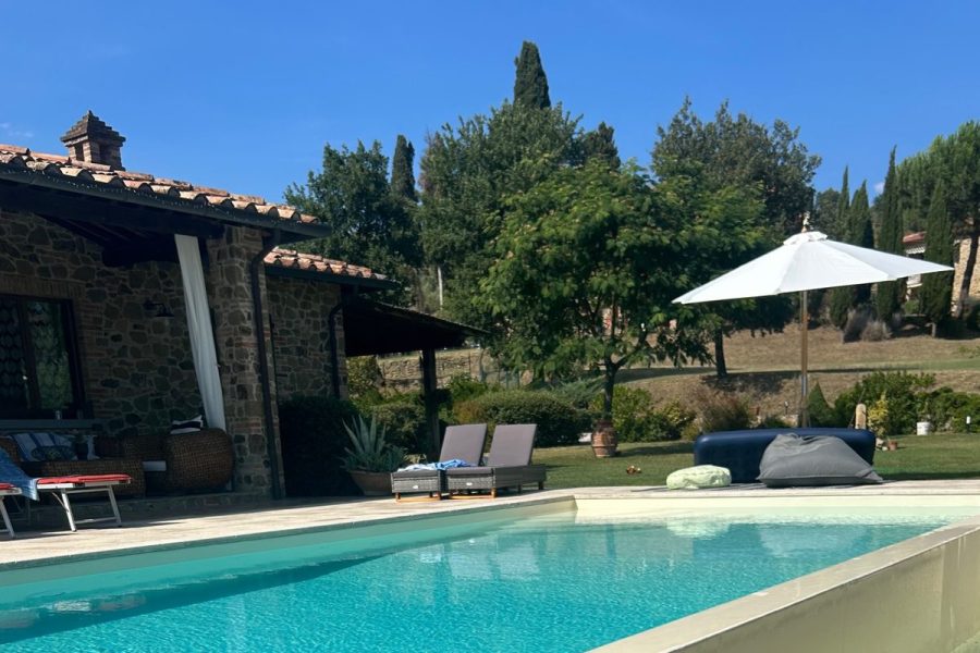 Piscina a sfioro con la parete del bordo verso il prato, davanti a una casa in pietra in Toscana