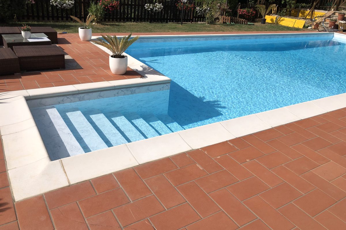 Piscina in mosaico azzurro con bordo bianco e pavimentazione in cotto