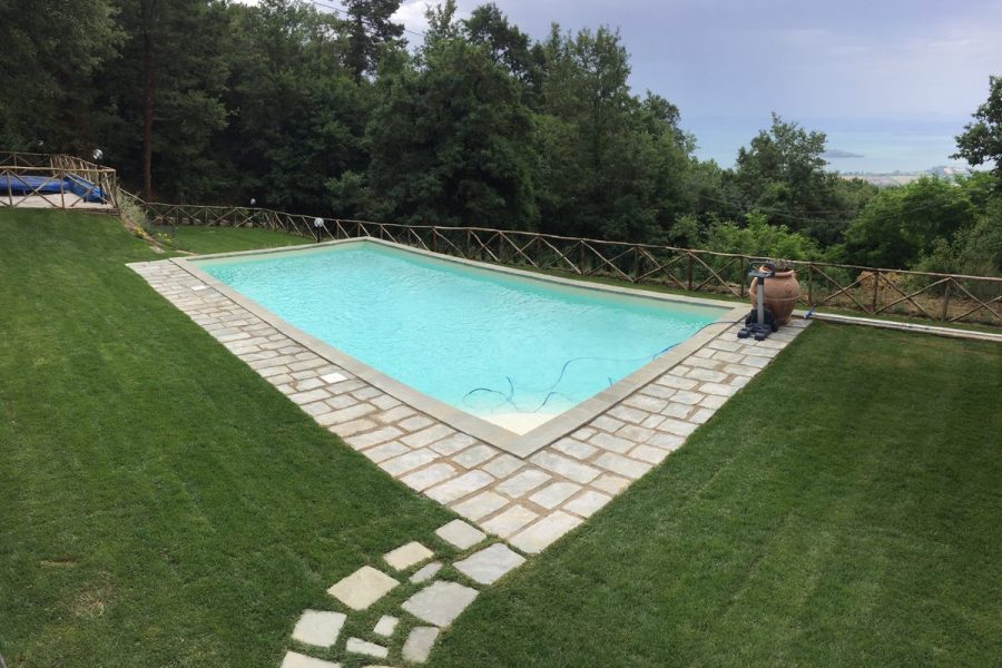 Piscina nel prato con bordo in cubetti di pietra e sentiero di lastre