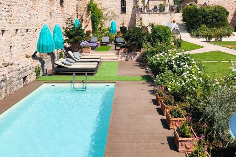 Piscina rettangolare con solarium e fioriere ai piedi delle mura della Rocca dei Trinci