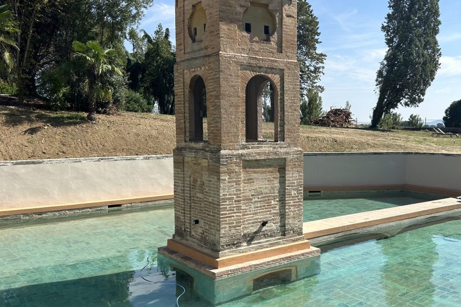 Torretta in mattoni al centro di una piscina, tra cipressi
